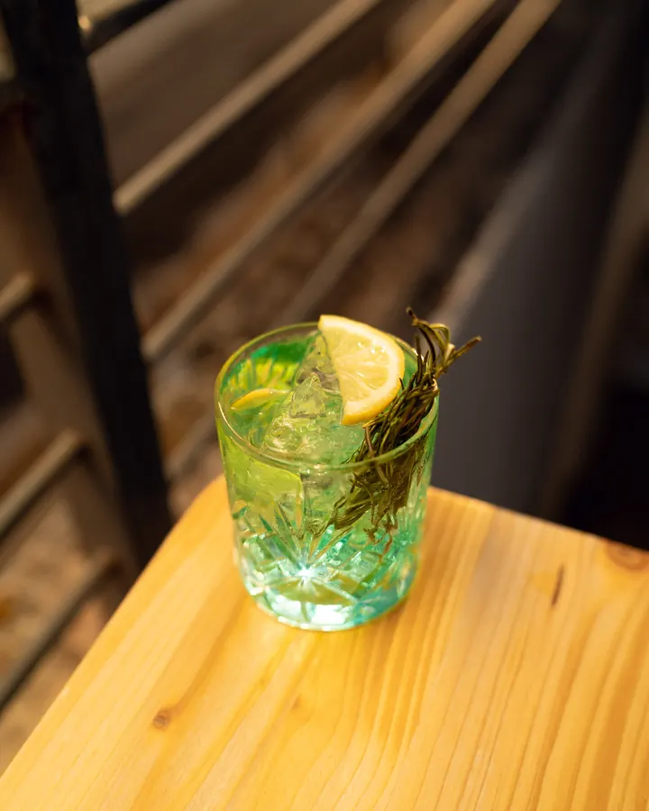 Gin tonic con rametto di rosmarino e fetta di limone sul tavolo di legno