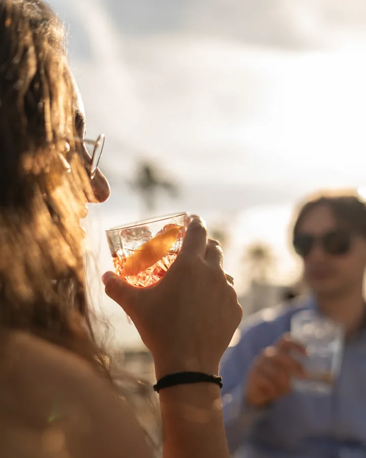 Un cocktail alzato controluce sulla terrazza, il mare dietro