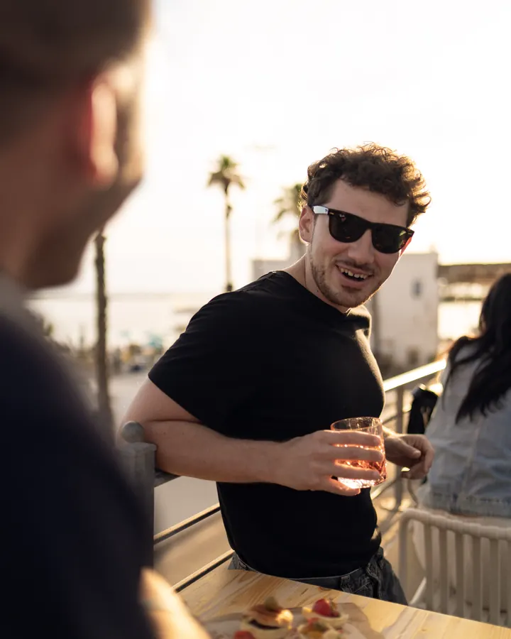Amici in piedi alla ringhiera della terrazza, il tavolo apparecchiato dietro